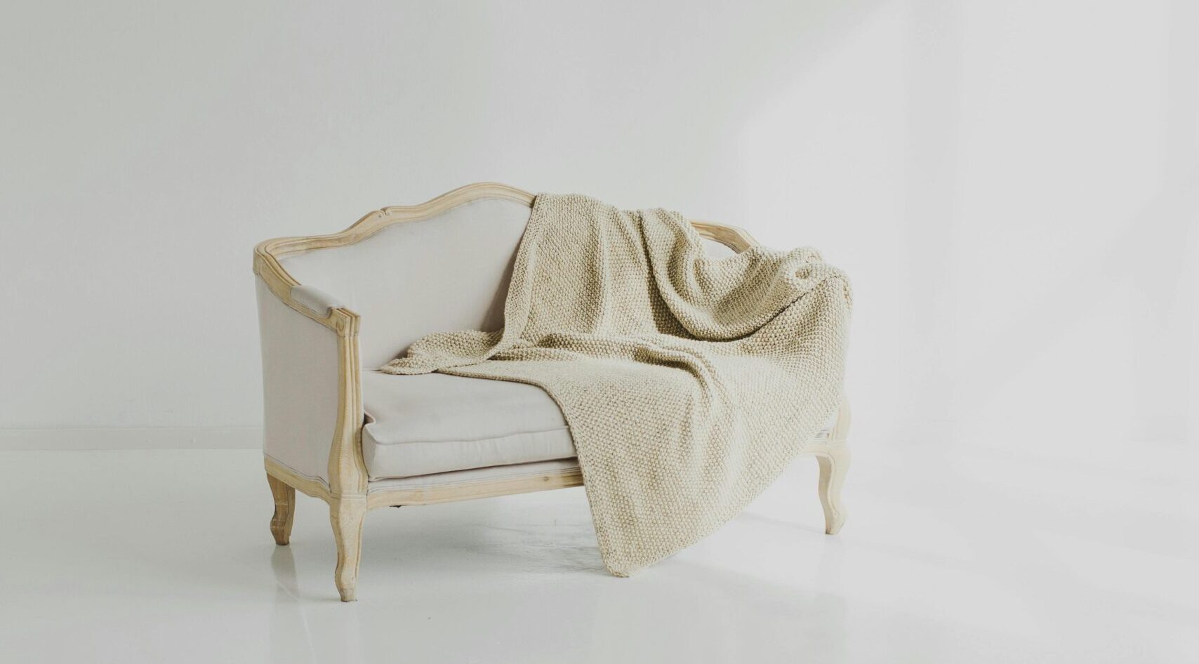 A beige throw on a vintage white sofa in a bright minimalist living space.