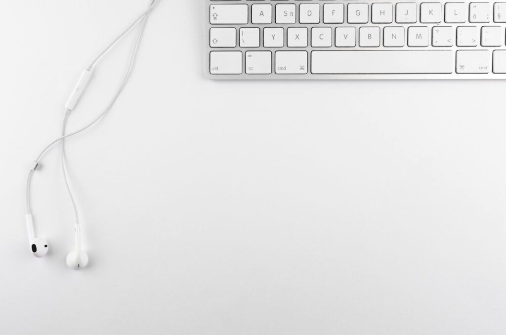 Top view of a minimal white desk setup featuring a keyboard and earphones on a clean background.